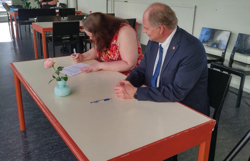 Kaksi henkilöä istumassa pöydän takana allekirjoittamassa paperia.