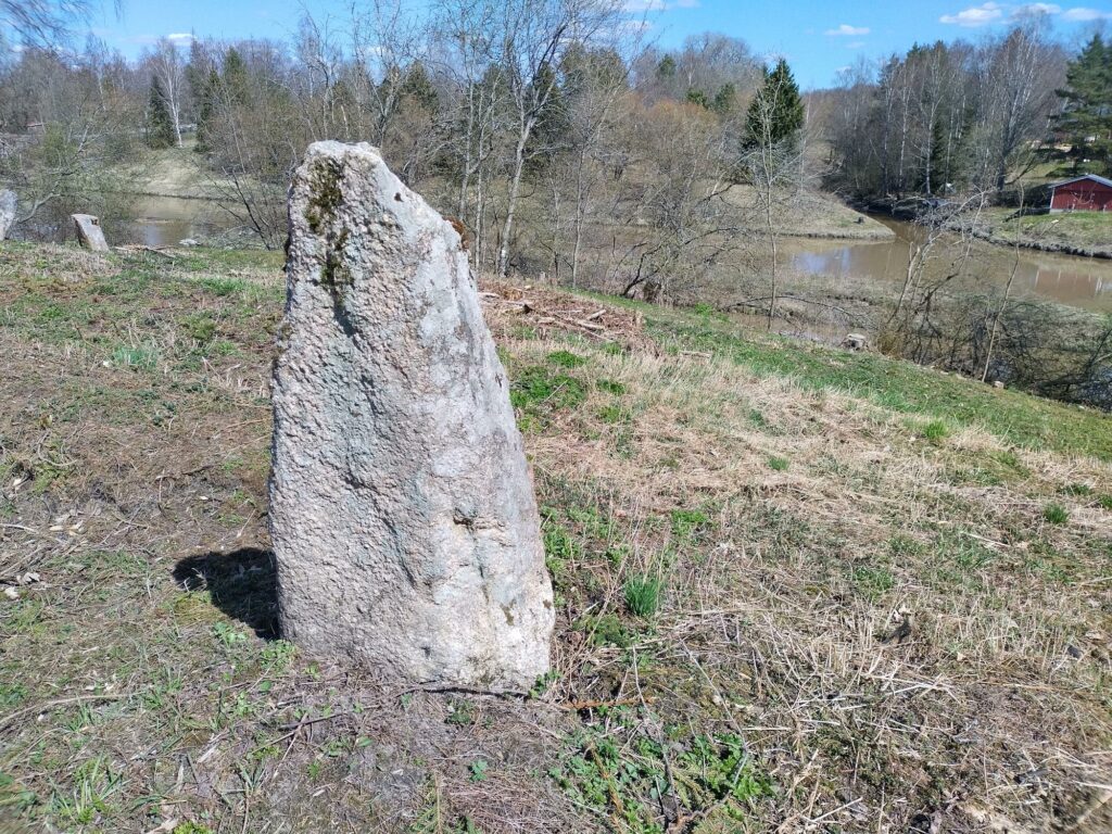 Kivinen hautamuistomerkki eli bautakivi jokeen viettävällä rinteellä.