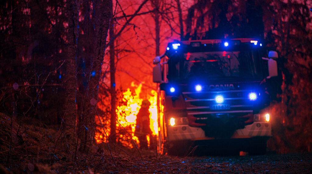 Etualalla paloauto ja takana palaa metsää sekä palomies.