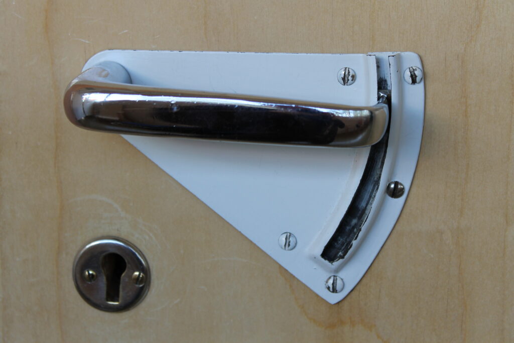 Metallinvärinen ovenkahva, jonka toinen pää kulkee urassa.