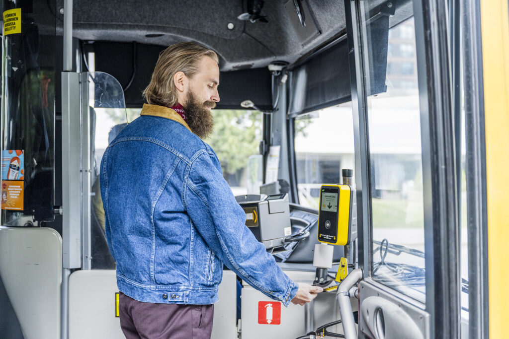 Mies maksamassa matkapuhelin avulla bussimatkaa bussissa.