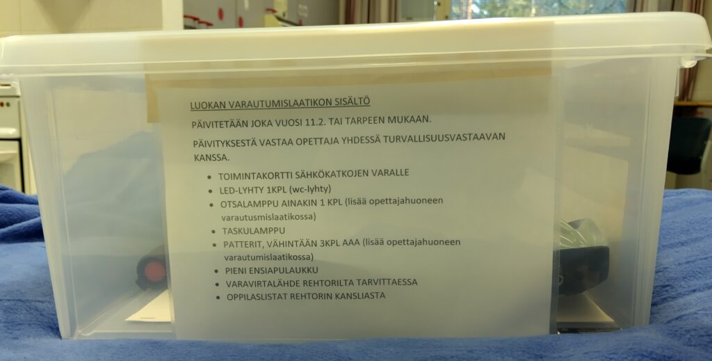 Koululuokan varautumislaatikon sisältö, kuten led-lyhty, otsalamppu, taskulamppu, pattterit ja pieni ensiapulaukku.